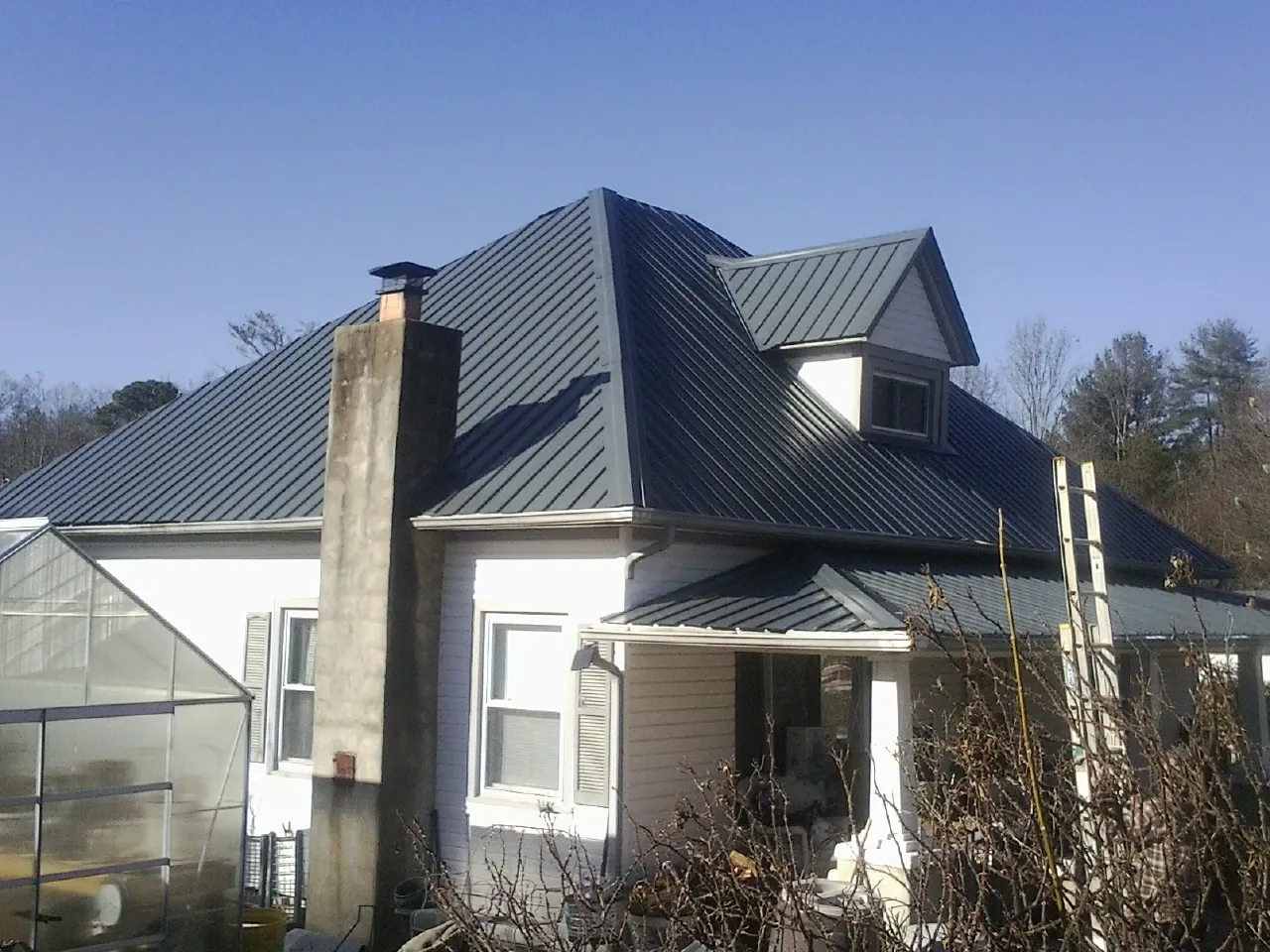 Dark blue standing seam metal roof on a white farmhouse with dormer — Slate & Tile Roof Repair by Roofing Brothers in Valentines