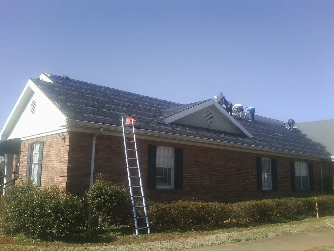 Crew tearing shingles off a brick ranch roof with a ladder set — Metal Roof Repair work by our crew in Valentines
