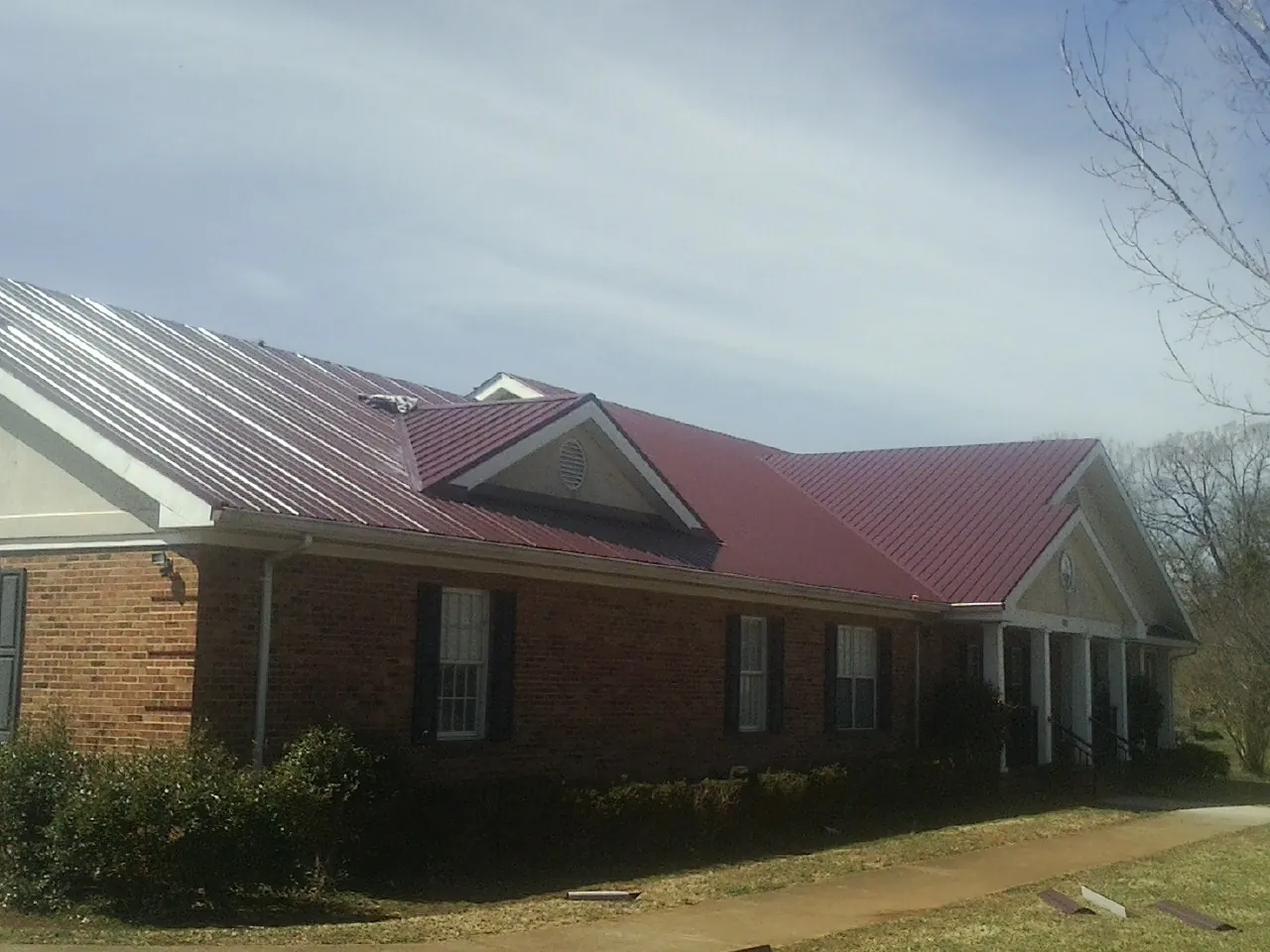 Red metal roof with gabled entries on a long brick building, from a Hail Damage Roof Repair job in Valentines