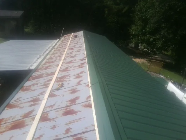 Old rusted panels beside newly installed green metal roofing — Wind Damage Roof Repair by Roofing Brothers in Valentines