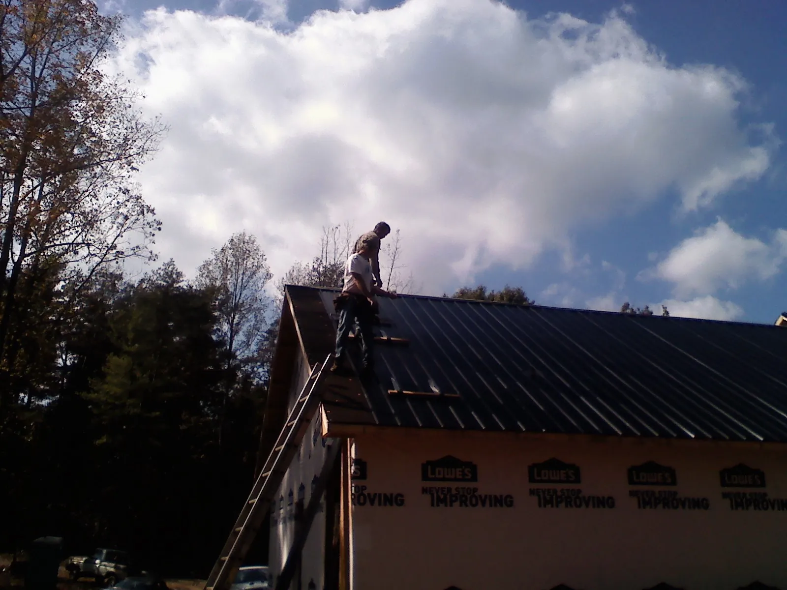 Roofer fastening dark metal panels high against a cloudy sky, from a Roof Inspection job in Valentines