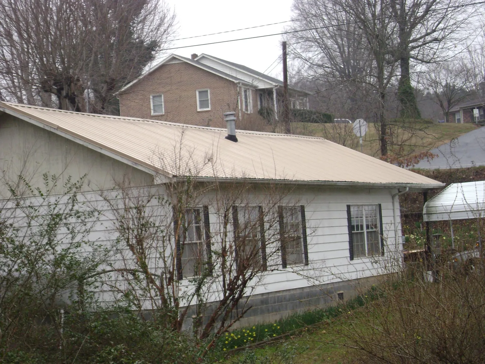 Tan metal roof on a white sided house set into a hillside — Commercial Roofing by Roofing Brothers in Valentines